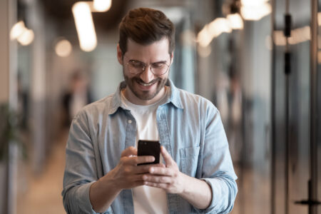 Happy Caucasian millennial male employee in glasses viewing mobile phone